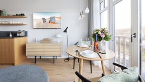 A modern kitchen with wooden cabinets, a dining area with a round table, and a large window with a view of the desert. - Dünenloft, House Kliff Whg. 5 (Sylt)