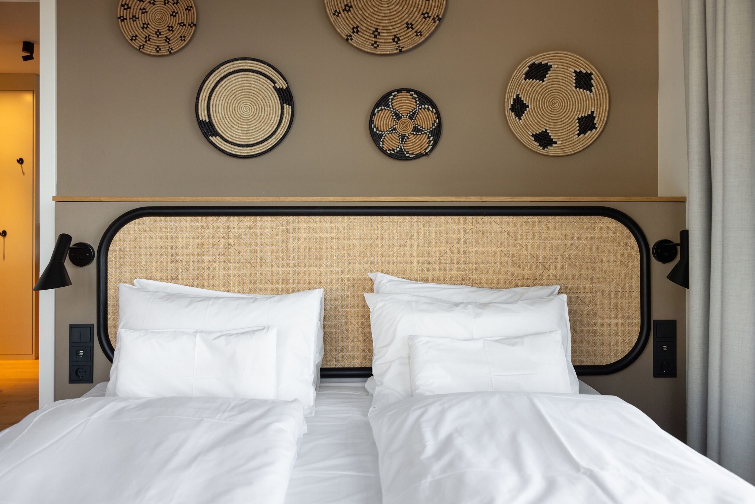 Une chambre d’hôtel comprenant un lit, deux assiettes décoratives fixées au mur et une tête de lit à la texture tissée.