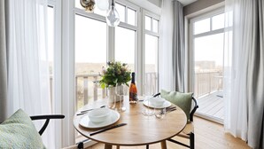 A dining area with a round table, chairs, a vase with flowers, wine glasses, and a bottle. - Dünenloft, House Kliff Whg. 5 (Sylt)