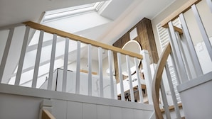 A modern interior with a skylight, white railings, and a wooden beam on the staircase. - Dünenloft, House Kliff, Whg. 9 (Sylt)