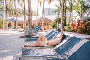 A resort area with lounge chairs, palm trees, and a building with a thatched roof. - Sunny Oasis | Swimming. Restaurant (Hollywood)