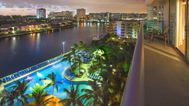 A waterfront hotel with a pool, palm trees, and a city skyline in the background. - Sunny Retreat | Restaurant + Outdoor Pool (Hollywood)