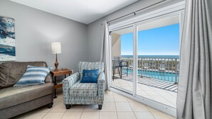 Ein Zimmer mit einer Couch, einem Sessel, einer Lampe und Blick auf einen Pool und einen Balkon.