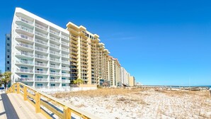 Ein Strandhotel mit mehreren Balkonen, einer Holzpromenade und einem Sandstrand.