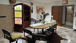 A dining area with a round table, chairs, and a view through an open door to an outdoor deck. - Bell Vivere Guesthouse (El Volcan)