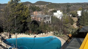 A swimming pool surrounded by trees and buildings, with a clear blue sky above. - Bell Vivere Guesthouse (El Volcan)
