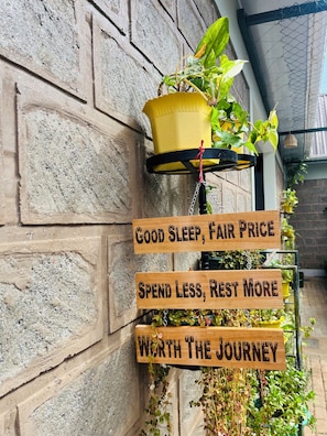 Une enseigne en bois ornée de phrases motivantes, un pot suspendu contenant des plantes vertes et un mur de briques.