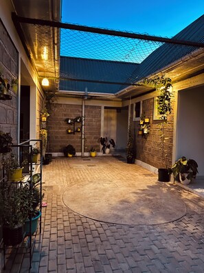 A courtyard with brick flooring, potted plants, and a metal fence. - Kili Haven Lodge (Moshi)