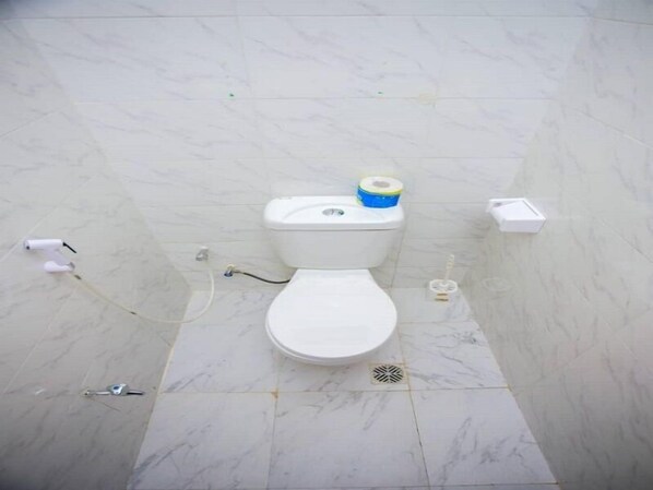 A bathroom with a toilet, a roll of toilet paper, and a small trash bin. - Kili Haven Lodge (Moshi)