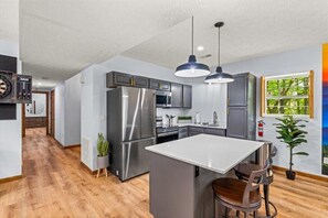 A modern kitchen with stainless steel appliances, a central island, pendant lighting, and a view of the outdoors through a window. - Private Hill~Luxury~Bowling~Special Events~Views~Hot Tub~Theater~Spa~Games~Gym (Sevierville)