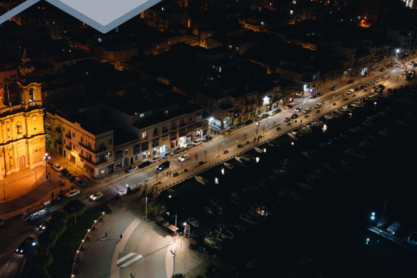 Ett flygbildsbild av en stadsgata på natten, med byggnader, bilar och en framträdande kyrka.