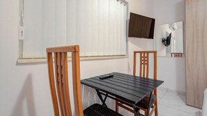 A small room with a wooden table and chairs, a window with blinds, a flat-screen TV mounted on the wall, and a wooden wardrobe. - Bright Msida Studio · King Bed - Fast WiFi (Msida)