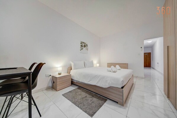 A modern bedroom with a bed, bedside tables, a desk, and chairs. - 1BR home with fully amenities, WIFI & AC in Msida (Msida)