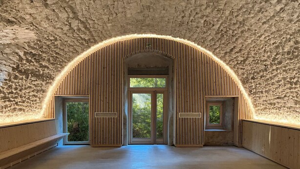 Une pièce à voûte, avec un mur en pierre à la texture particulière et des lambris en bois.