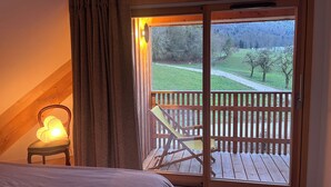 Une chambre dotée d’une grande porte-fenêtre coulissante donnant sur un balcon avec une terrasse en bois et une chaise.