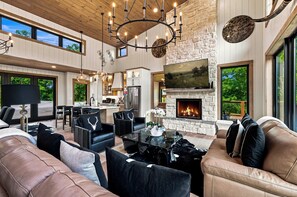 A spacious living area with a fireplace, leather sofas, and a dining area with a kitchen in the background. - Beneath the Stars | Luxury 3BR Cabin w/ Indoor Pool & Game Room (Gatlinburg)