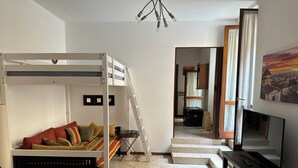 Een knus woongedeelte met een stapelbed, een eettafel met een fles en glazen, een televisie en een trap naar een andere kamer.