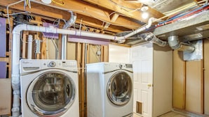A laundry room with two front-loading washing machines, wooden beams, and exposed ductwork. - Walk to Shops at Belmar: Denver Area Home Base (Lakewood)