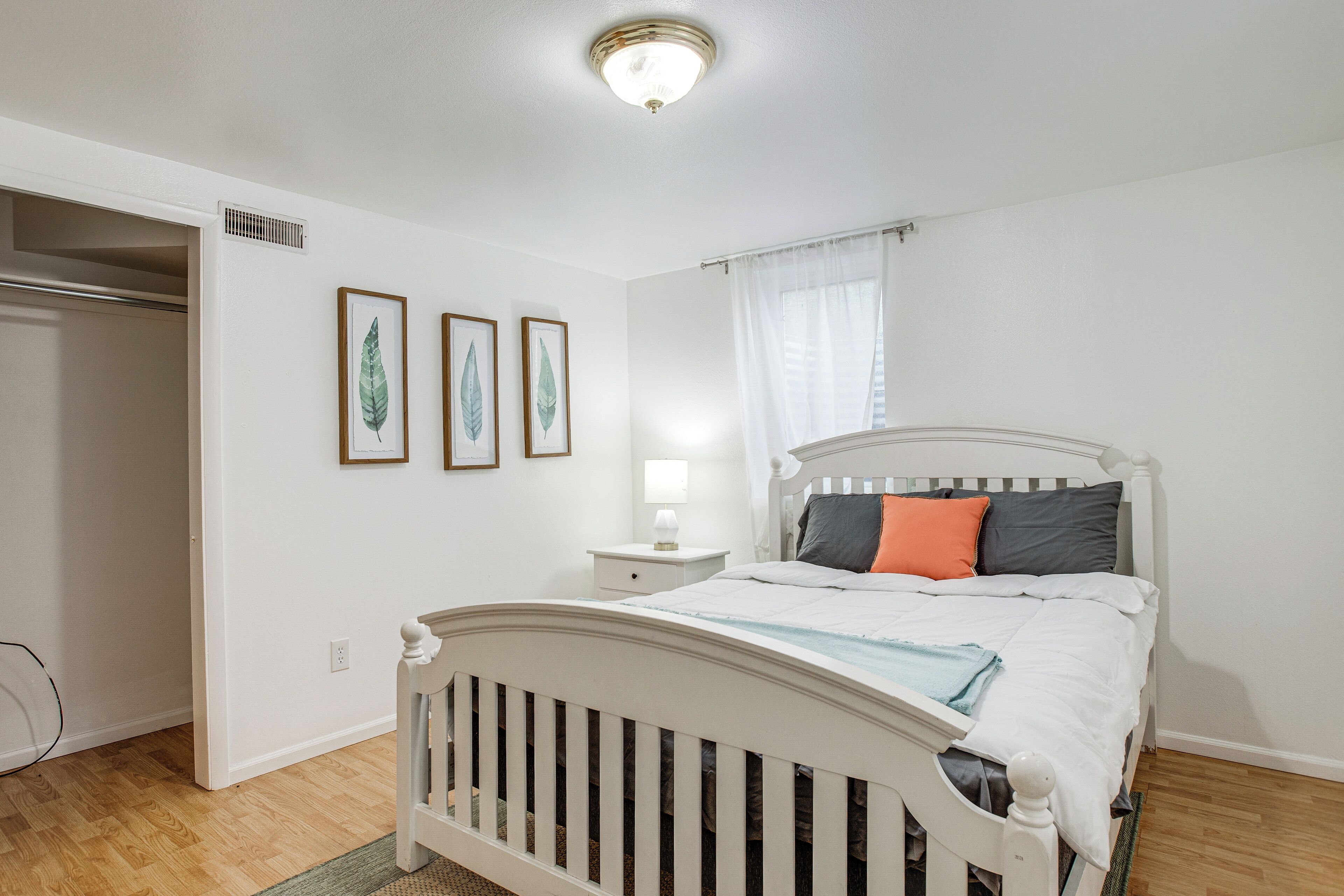 A bedroom with a white bed, a nightstand, a lamp, and three framed leaves on the wall.