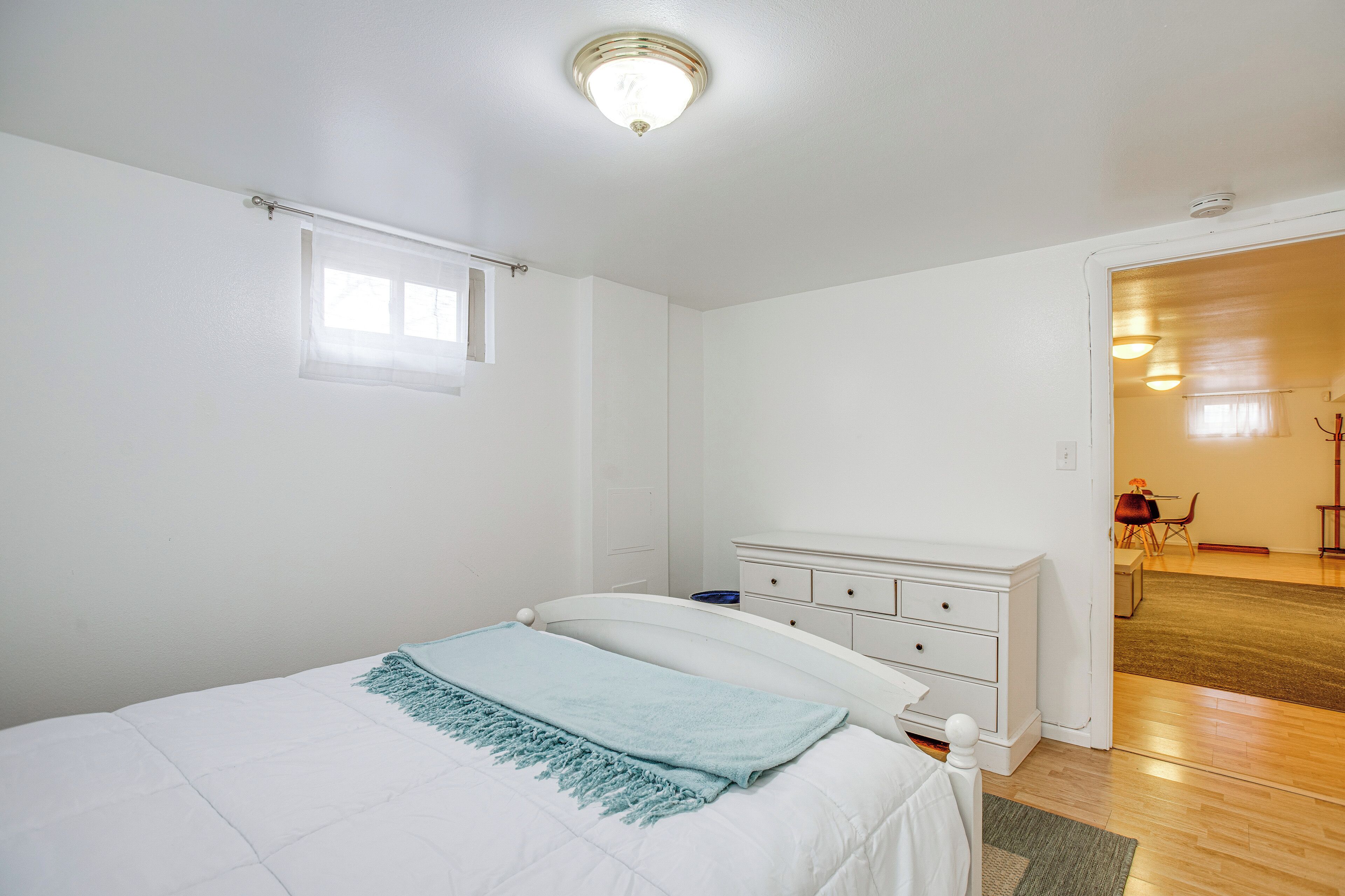 A bedroom with a bed, a dresser, a window, and a door leading to another room.