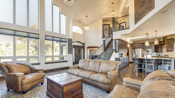 A spacious living area with leather sofas, a wooden coffee table, and a large rug. A staircase leads to a kitchen area with modern appliances and a dining table. - Hot Tub & Games Galore! Colorado Springs Retreat (Colorado Springs)