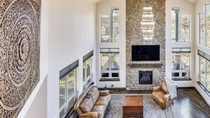 A spacious living room with a stone fireplace, leather sofas, and large windows offering views of the outdoors. - Hot Tub & Games Galore! Colorado Springs Retreat (Colorado Springs)