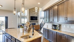 A spacious kitchen with granite countertops, dark wooden cabinets, and a stone accent wall. - Hot Tub & Games Galore! Colorado Springs Retreat (Colorado Springs)
