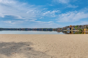 A sandy beach with a calm lake and a row of houses in the background. - < 1 Mi to Lake Winnipesaukee: Family Winter Escape (Moultonborough)