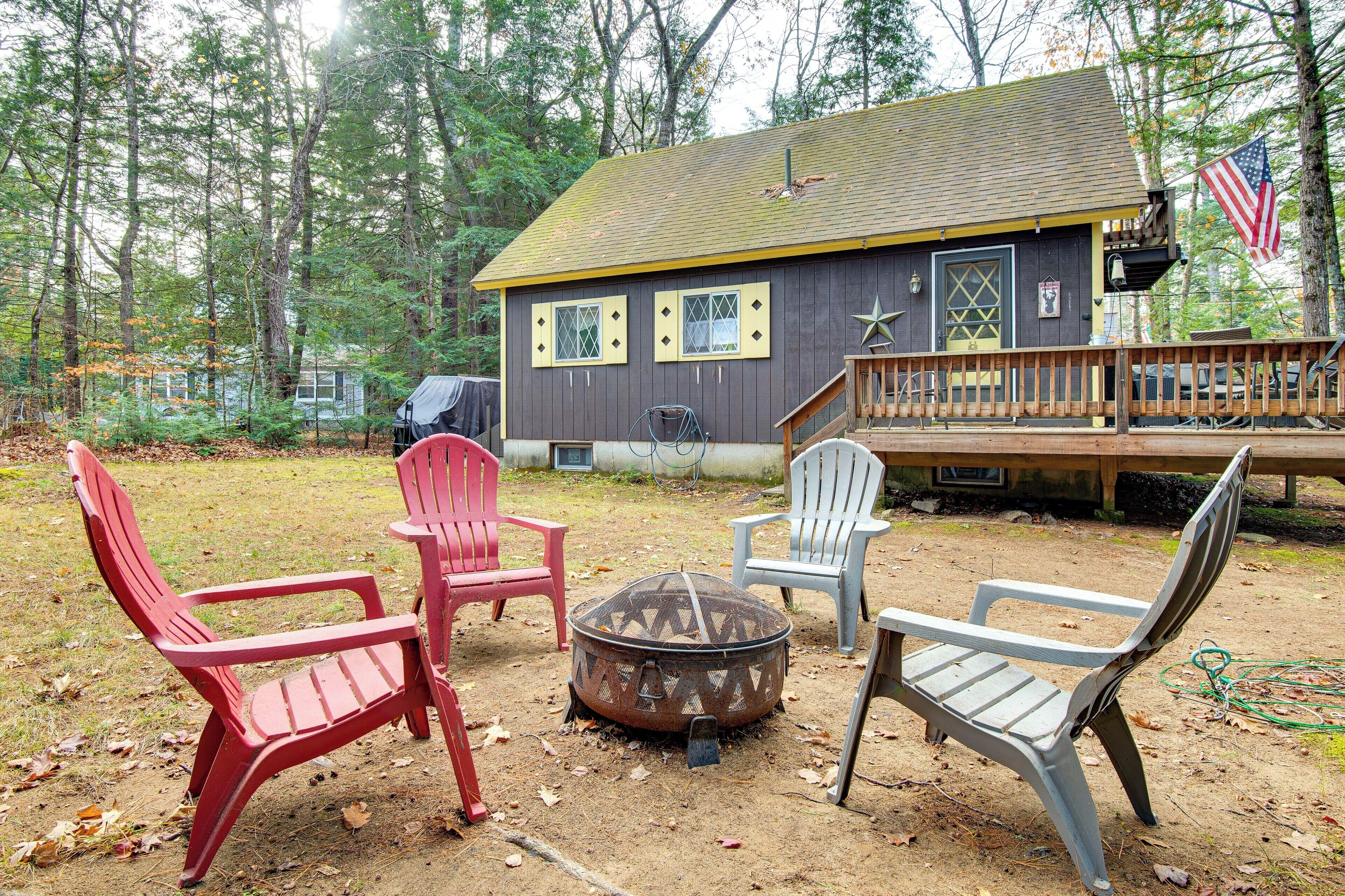 A cabin with a deck, a fire pit, and Adirondack chairs.