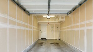 Eine saubere, leere Garage mit einer weißen Tür am Ende, einer Metallleiter und einer Deckenleuchte.