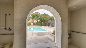 Ein Poolbereich mit Blick durch einen Rundbogen, einer gefliesten Wand und einem Metallgeländer.