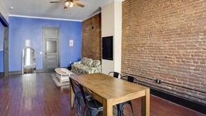 Un comedor con una mesa y sillas de madera, un ventilador de techo y una pared de ladrillo.