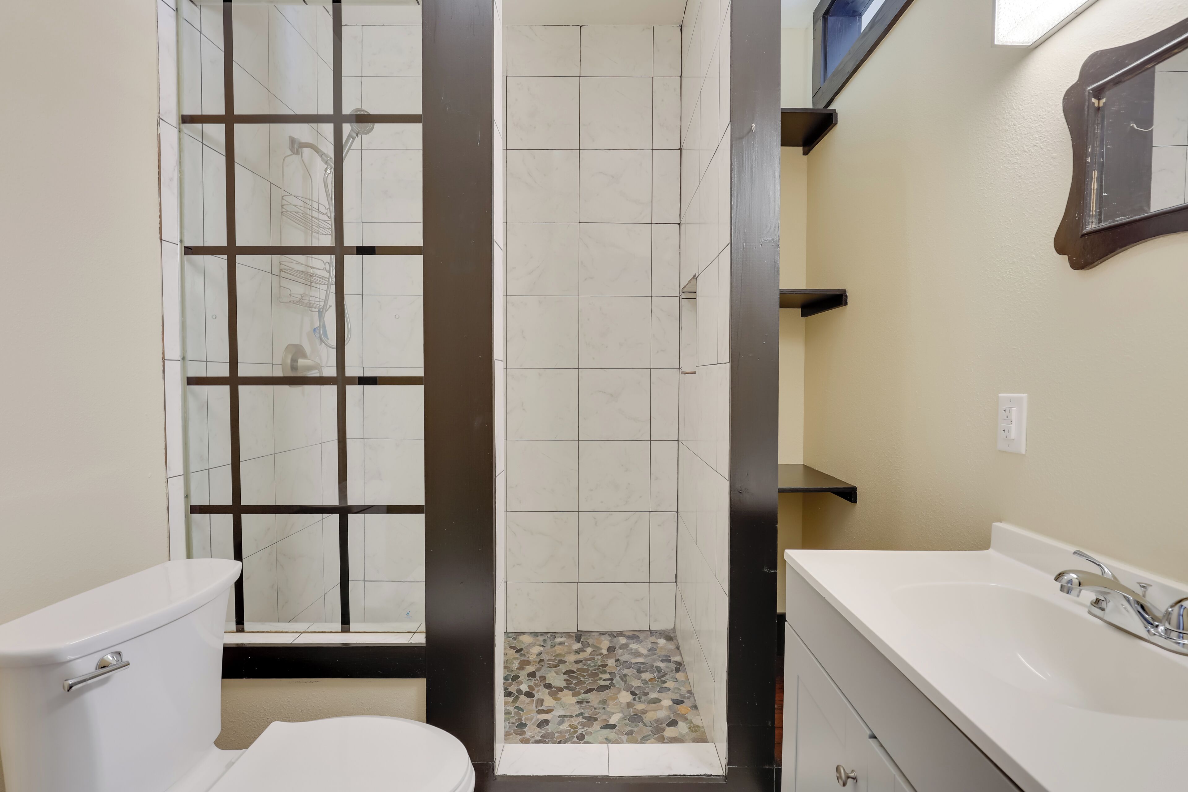 A bathroom with a toilet, a shower with a tiled floor, and a sink with a mirror.
