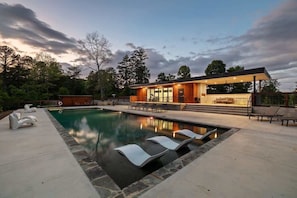 Une maison moderne dotée d’une piscine, de chaises longues et d’un patio couvert.