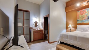 A hotel room with a bed, bedside table, TV, wooden wardrobe, bathroom, and a painting on the wall.