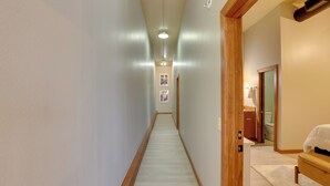 A narrow hallway with a wooden floor, a light fixture, and a door leading to a bathroom.