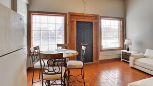 A dining area with a wooden table and chairs, a black door, and a white sofa in a room with wooden flooring and large windows.