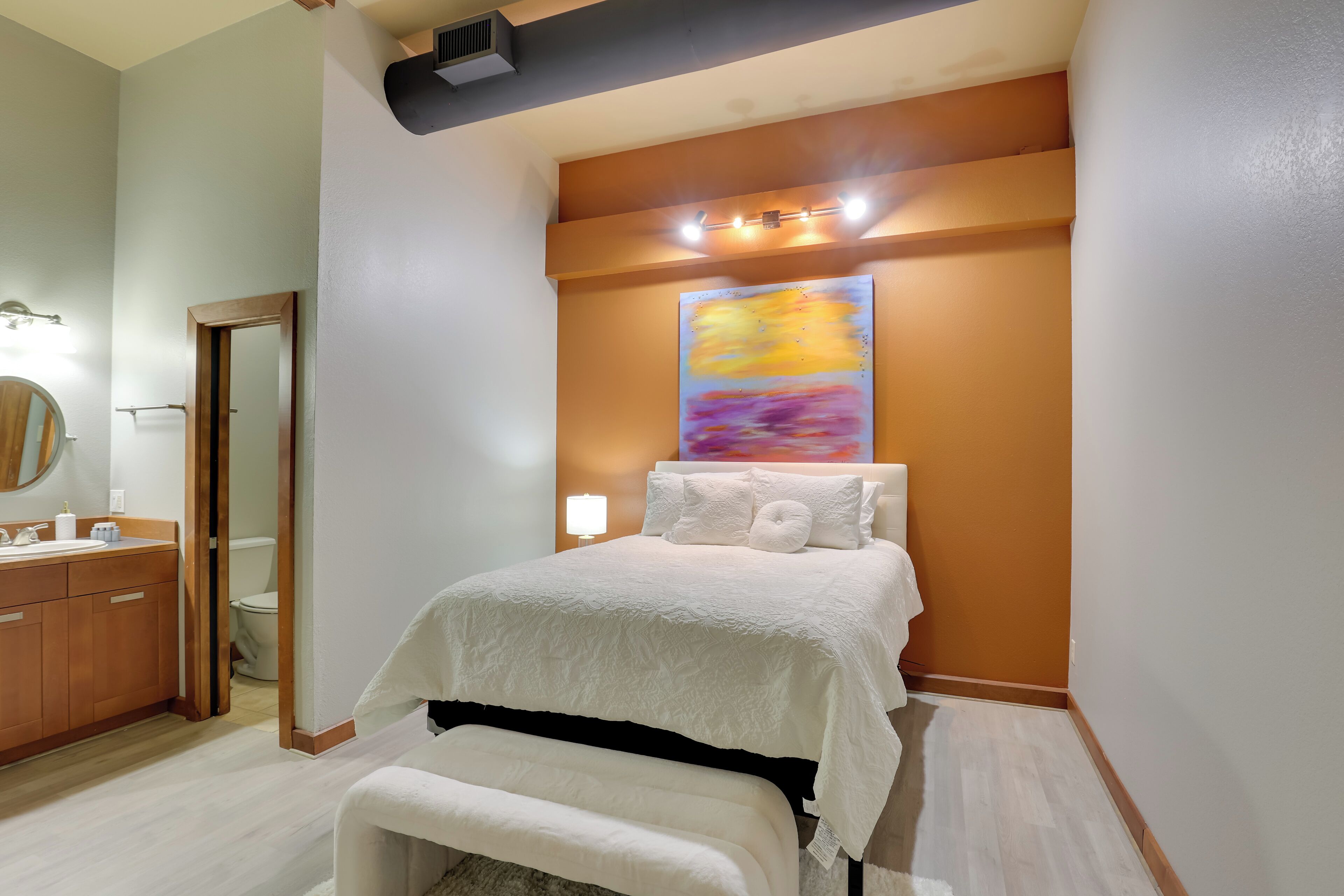A bedroom with a bed, a nightstand, a mirror, a wooden dresser, and a painting on the wall.