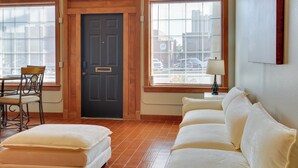 A room with a wooden door, a sofa, a chair, and a window with blinds.
