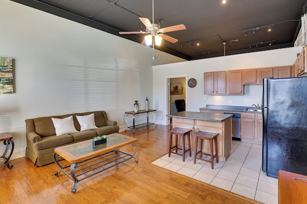 A modern kitchen with wooden cabinets, a black refrigerator, and a dining area with stools.