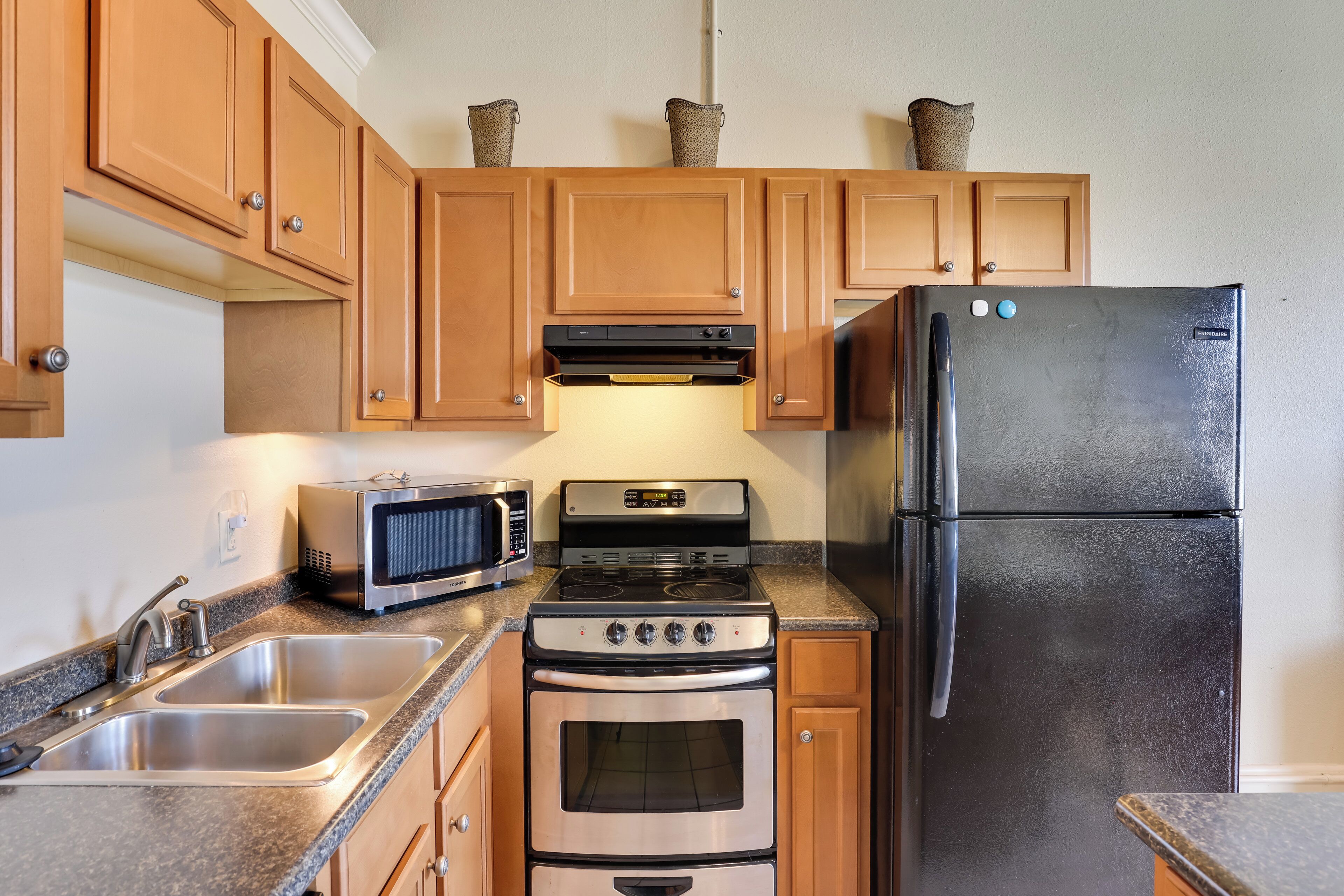 A kitchen with wooden cabinets, stainless steel appliances including a refrigerator, microwave, and oven.