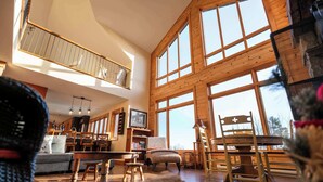 Un salón amplio con techo alto, ventanas grandes, una escalera de madera y una chimenea acogedora.