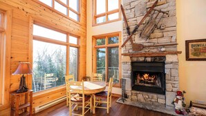 Un interior de cabaña acogedor, con chimenea de piedra, mobiliario de madera y ventanas amplias.