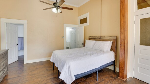 Un dormitorio con cama de madera, ventilador de techo y puerta que da a otra habitación.