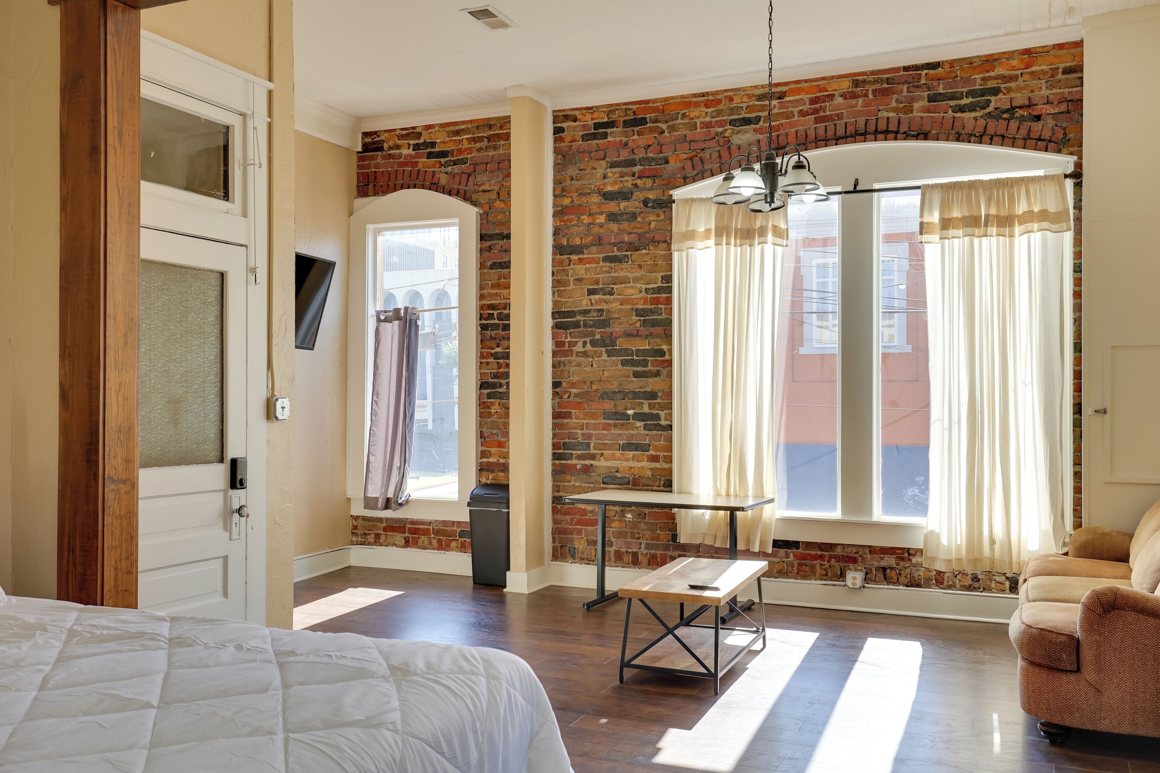 Une pièce avec un mur en briques, un lit, une table, une chaise et une fenêtre avec des rideaux.