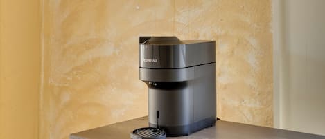 A modern espresso machine on a wooden table against a textured wall.