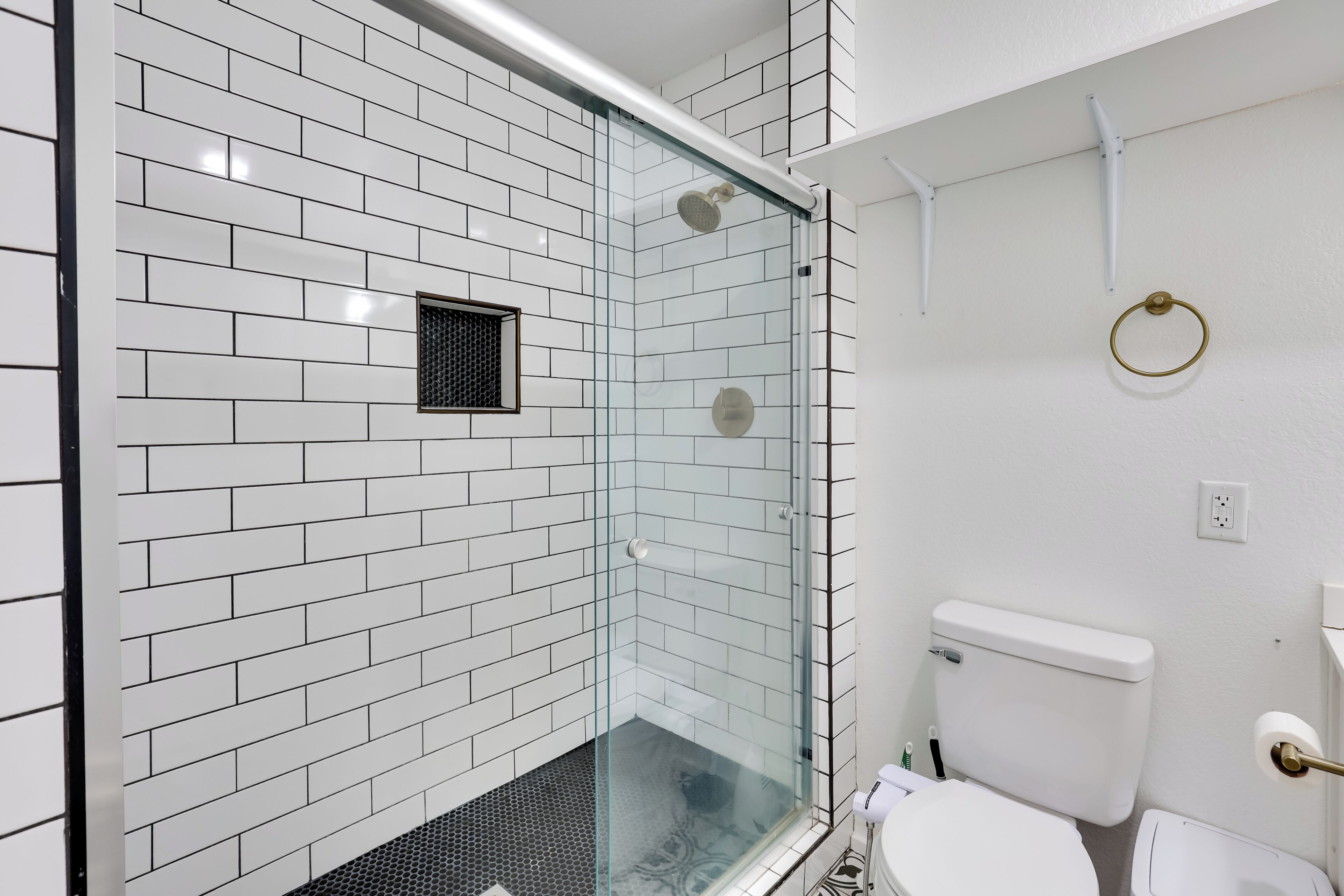 Un bagno moderno con piastrelle bianche a metro, box doccia in vetro, un water e una piccola finestra.