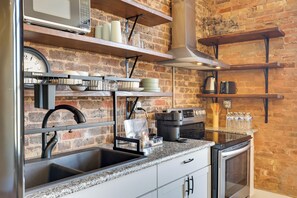 A kitchen with a brick wall, stainless steel appliances, and wooden shelves. - Shop, Dine & Unwind at Historic Dtwn Marshall Apt (Marshall)