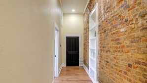 A hallway with a wooden floor, a brick wall on one side, and a white door at the end. - Shop, Dine & Unwind at Historic Dtwn Marshall Apt (Marshall)