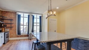 A kitchen with a large island, wooden flooring, and a brick accent wall. - Shop, Dine & Unwind at Historic Dtwn Marshall Apt (Marshall)